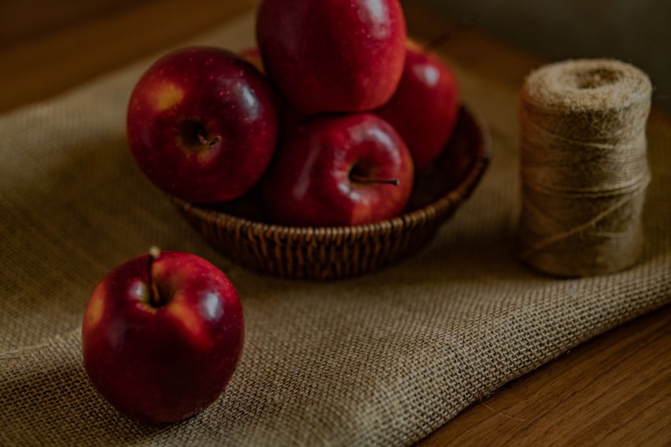 A rustic setup featuring red apples in a wicker basket on burlap.