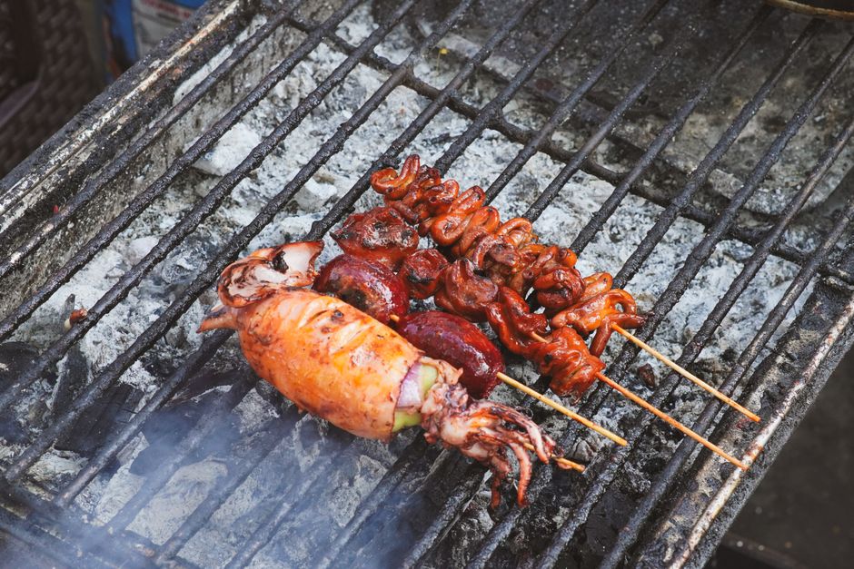Close-up of various seafood skewers grilling on a traditional charcoal barbecue.