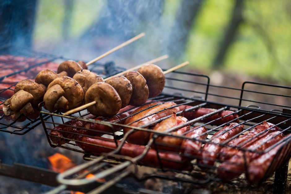 Delicious skewered mushrooms and sausages grilling over charcoal on a barbecue grill outdoors.