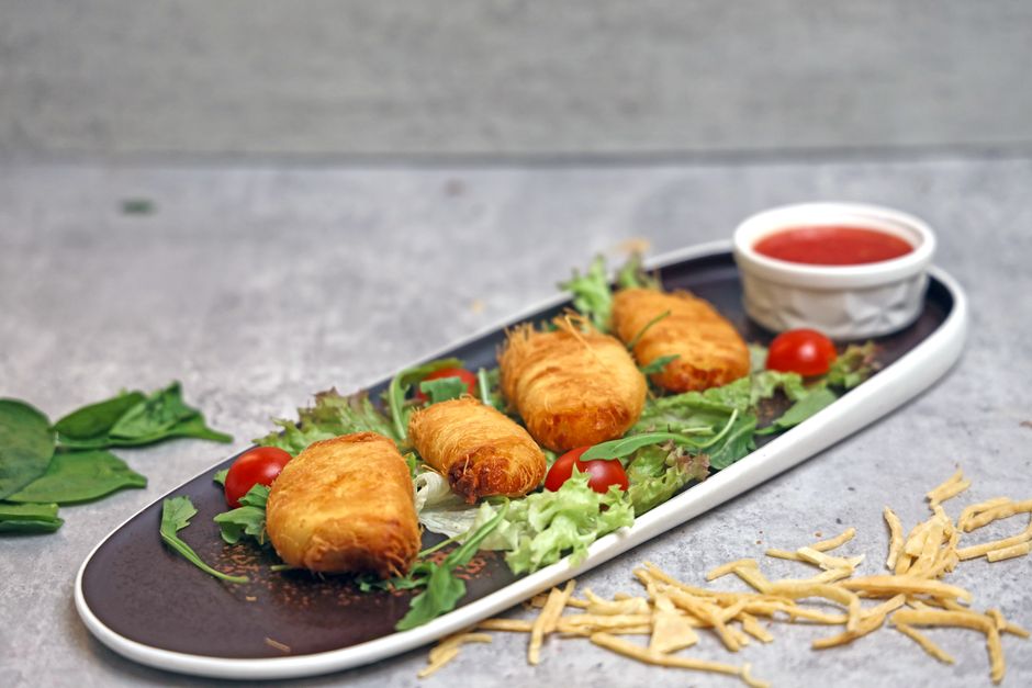 Crispy rolls served on a stylish plate with fresh greens and a tomato dip.