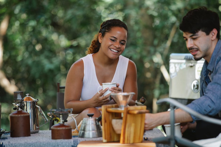 Joyful diverse young couple sitting at table in nature and brewing fresh coffee during romantic picnic on sunny day