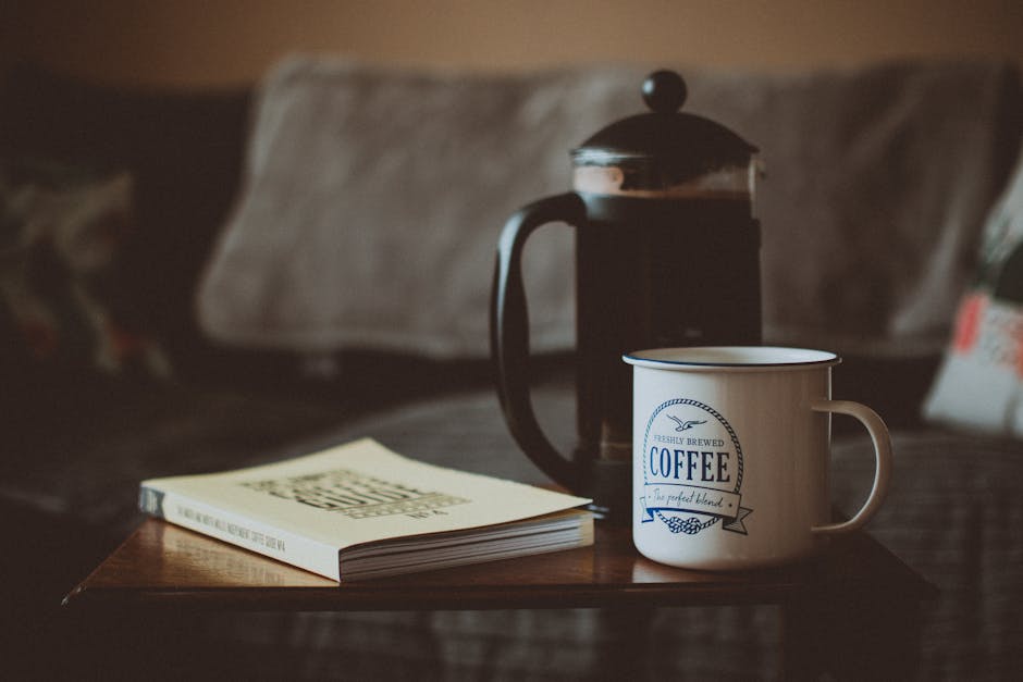 A warm setting with a coffee cup, book, and French press on a table.