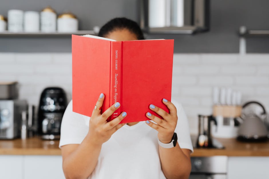 Woman reading a red book in a stylish kitchen. Perfect for lifestyle and leisure themes.