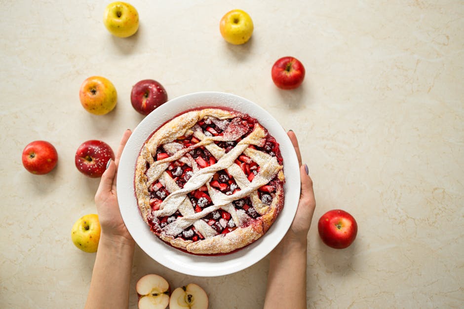 Hands holding a freshly baked fruit pie surrounded by apples on a light surface. Perfect for autumn themes.