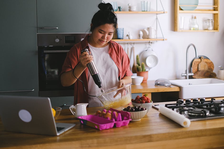 Woman using a mixer in a modern kitchen, preparing food with fresh ingredients.