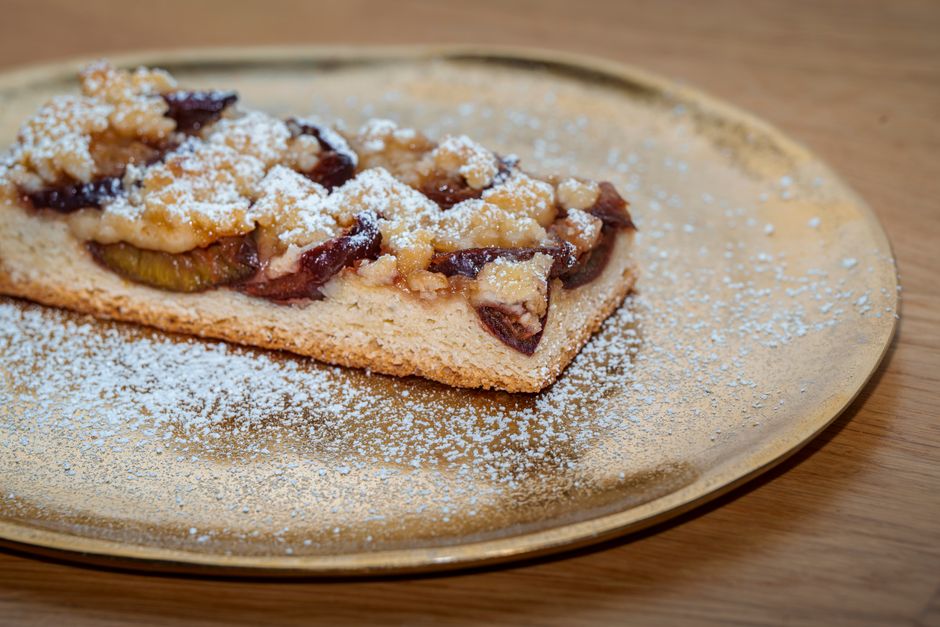 Plum tart with a crumble topping on a golden plate, dusted with powdered sugar.