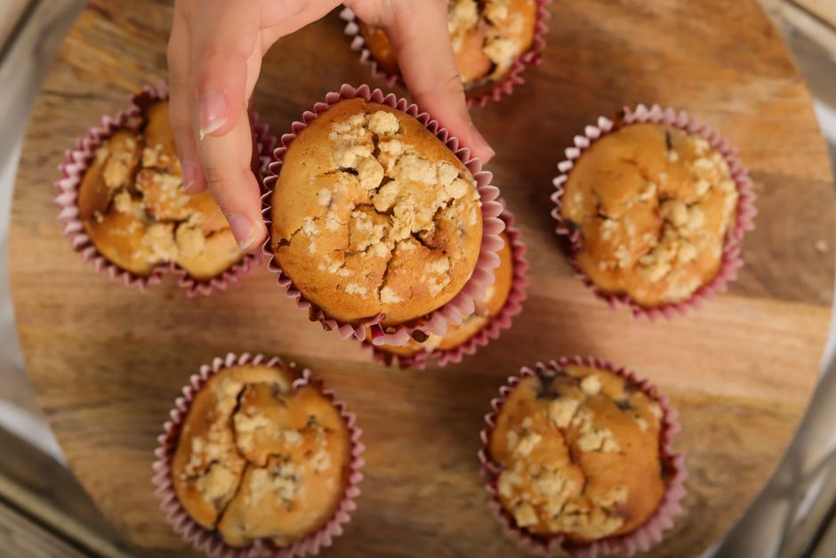 Hand picking a freshly baked muffin from a group on a wooden platter.