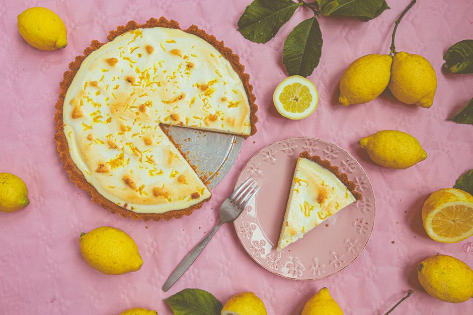 Top view of a lemon tart with fresh lemons on a pink background, perfect for dessert inspiration.