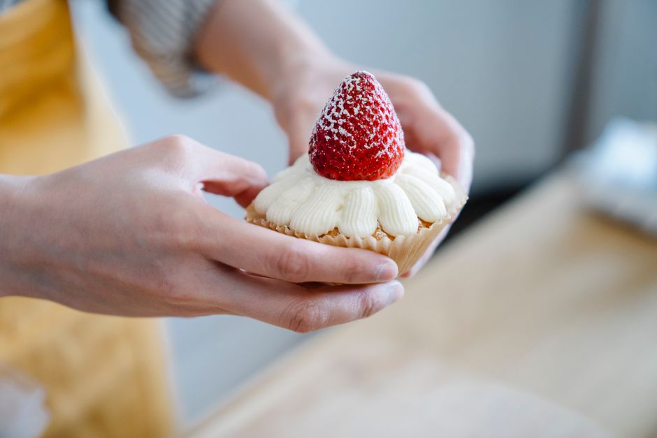 Close-up of hands holding a sweet cupcake topped with cream and a fresh strawberry.