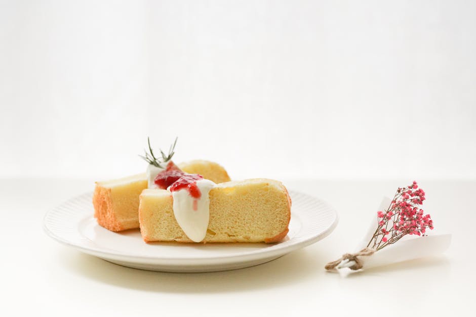 Slice of sponge cake with cream and berry topping on a white plate with floral garnish.