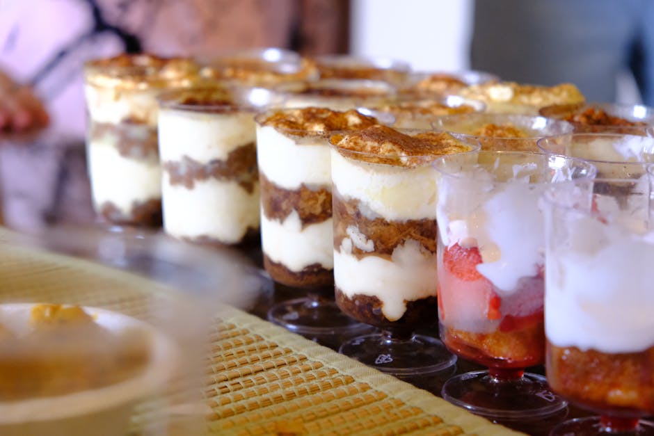 A selection of layered dessert cups, including tiramisu and fruit parfait, displayed on a table.