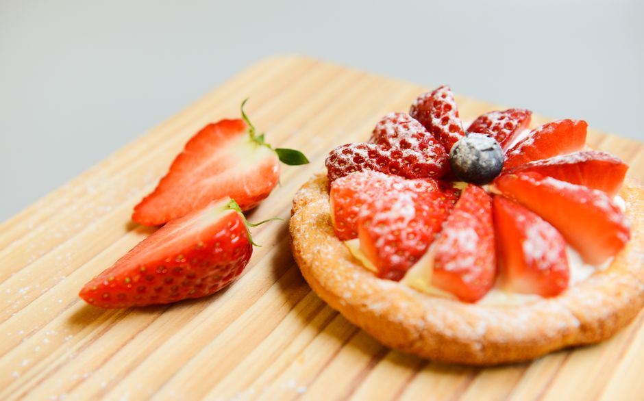 A delightful strawberry tart with fresh cream and powdered sugar served on a wooden board.