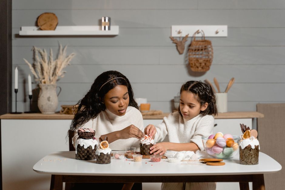 An African American woman and a Hispanic girl creatively decorate cupcakes in a cosy indoor setting.