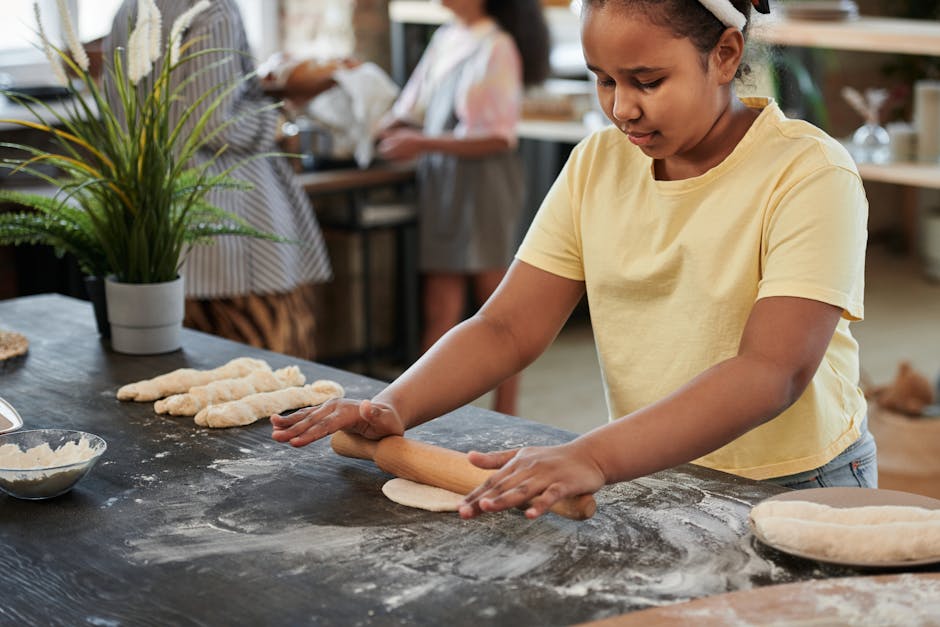 A young girl rolls dough with a rolling pin in a bakery setting, surrounded by baking ingredients.