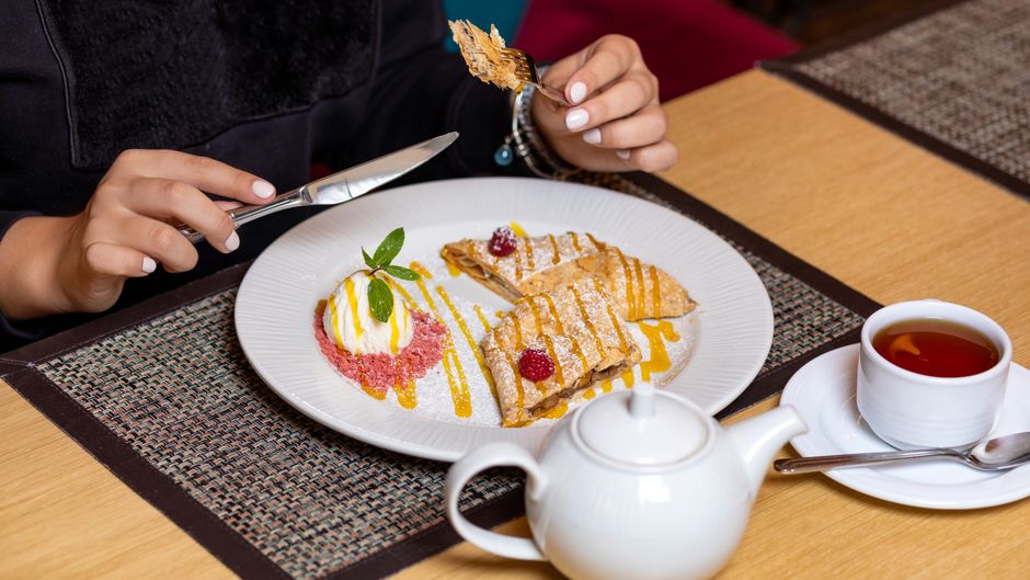 A close-up of a person enjoying a delicious dessert and tea in a cozy setting.
