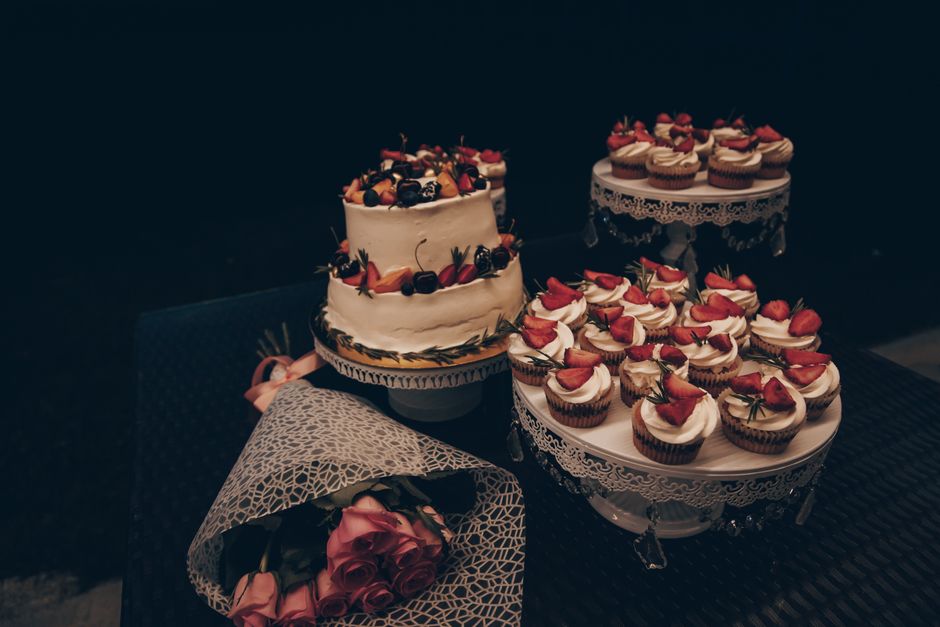 Elegant cake and cupcake display garnished with fruits and roses, perfect for celebrations.