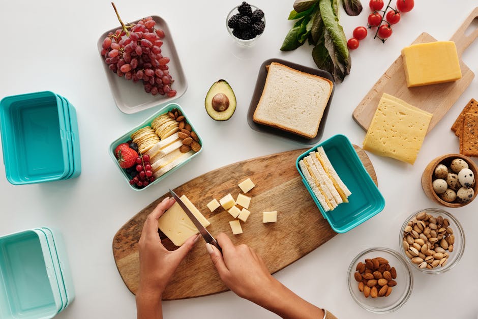 Top view of a person preparing a cheese and fruit spread with various ingredients on wooden board.
