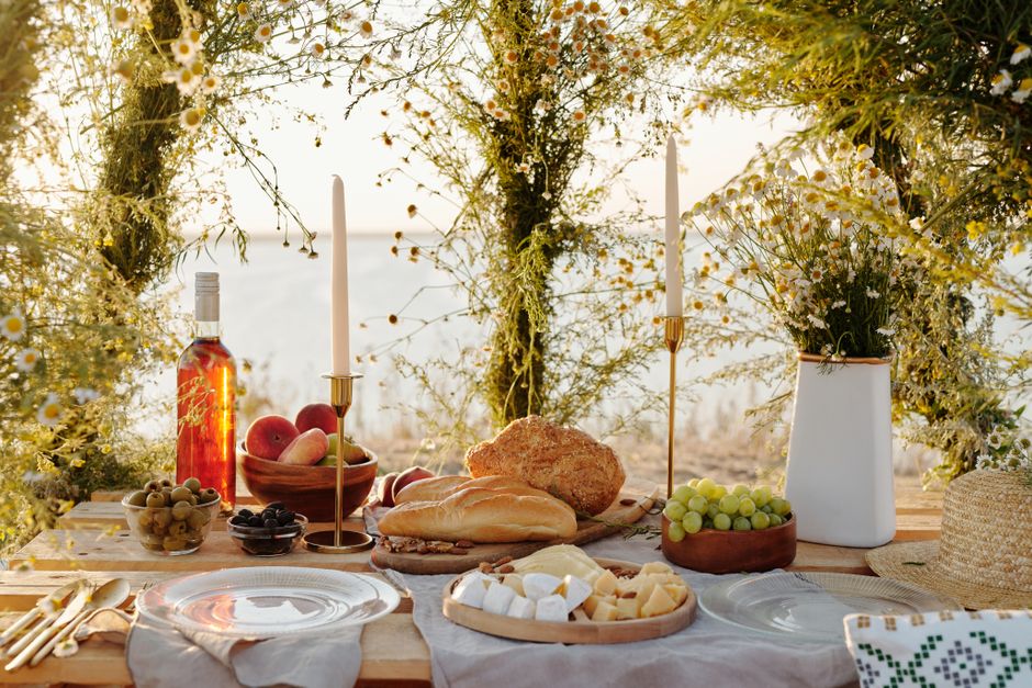 Charming picnic setup with fresh fruits, cheese, and flowers by the lake at sunset.