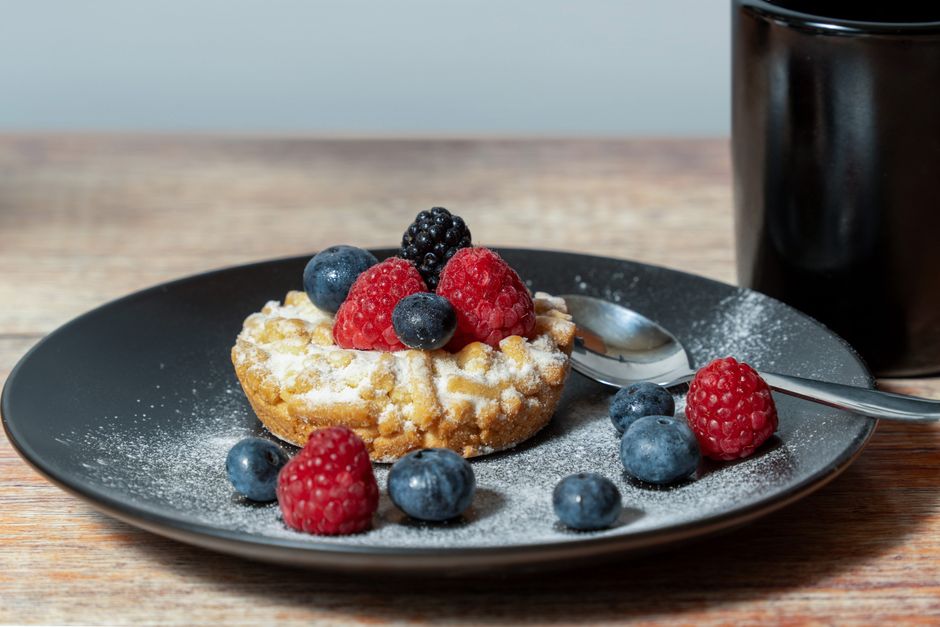 Close-up view of a pastry with mixed berries and powdered sugar on a black plate with a spoon.