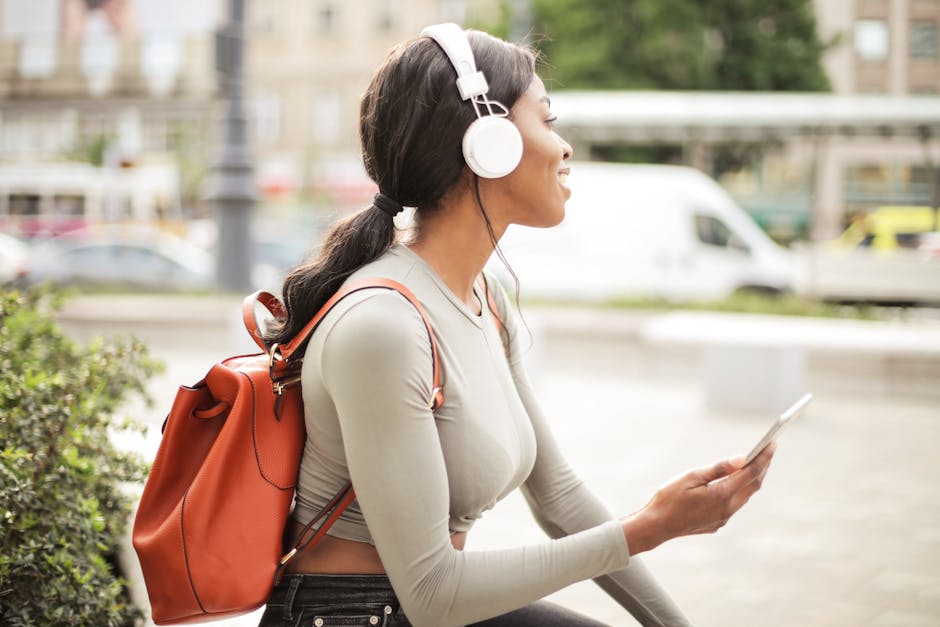 A woman wearing headphones and a backpack sits outdoors, enjoying music on her smartphone.