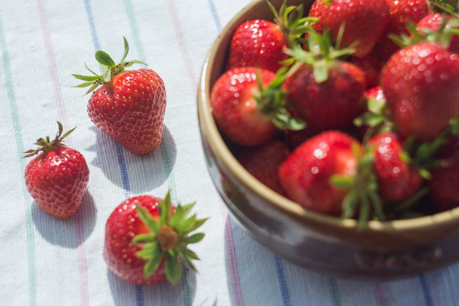 Vibrant fresh strawberries in a ceramic bowl and on a striped tablecloth in natural lighting.