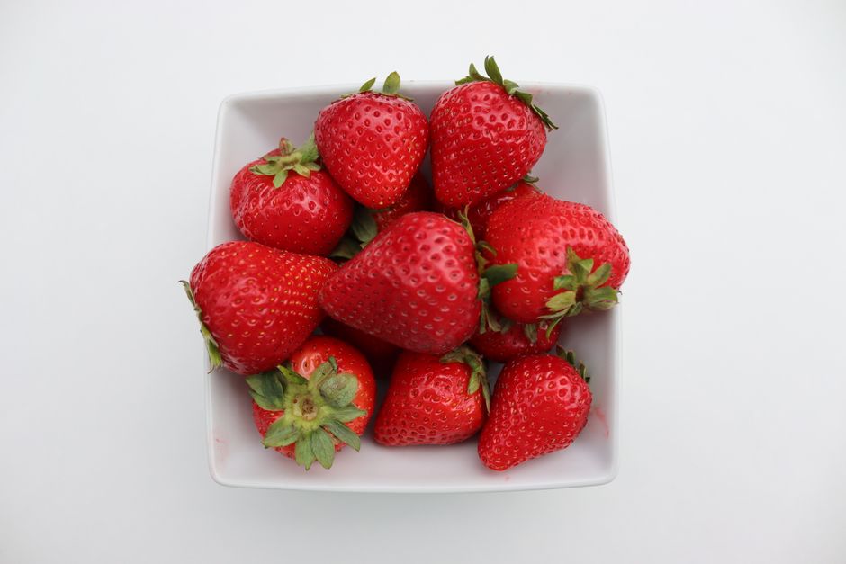 A close-up view of ripe strawberries in a square white bowl, showcasing vibrant red colors.