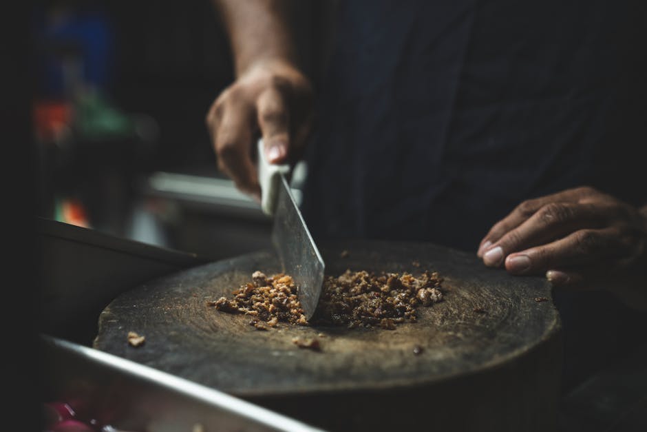 A person slicing food on a wooden chopping board with a knife, capturing culinary preparation in action.