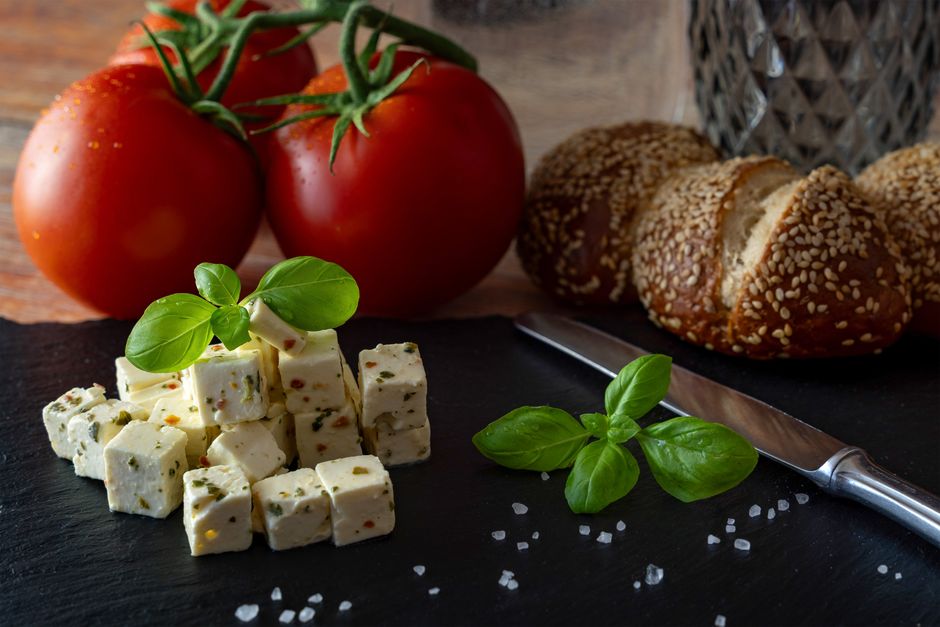 Fresh antipasti featuring cheese cubes, basil, tomatoes, and bread on a black slate.