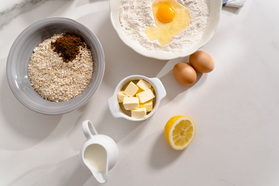Overhead shot of baking ingredients like flour, eggs, and lemon on a white surface, ready for preparation.